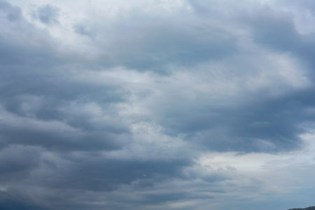 Dark storm clouds gather across the blue sky during the rainy season, forming dramatic shapes as...