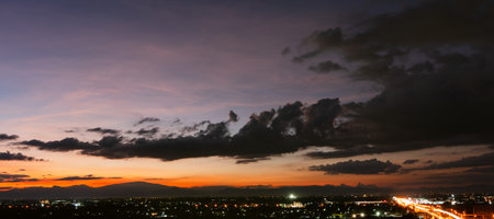 Twilight falls over Lamphun province, soft orange and purple hues paint the sky above the mountains while city lights and gentle traffic beautiful evening in a wide-angle view.の写真素材