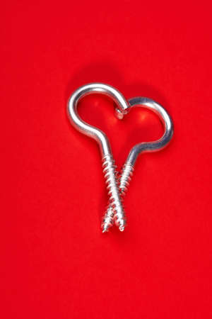 Two spiral bolts laying in the form of heart on a red backgroundの写真素材