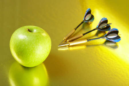 Apple and the three darts laying on a golden background の写真素材