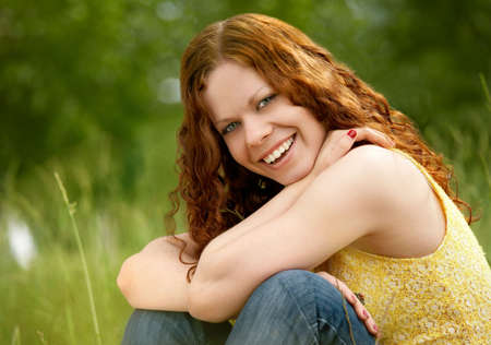 A smiling girl sits on a background of trees and grassesの写真素材