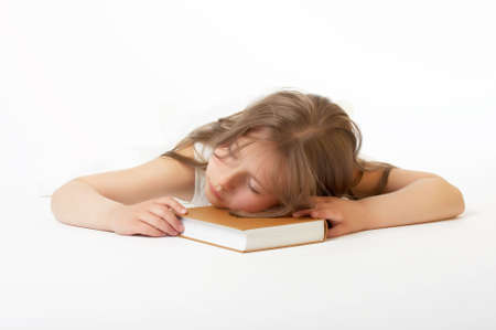 The little girl sleeps, having put a head on the book on a white backgroundの写真素材