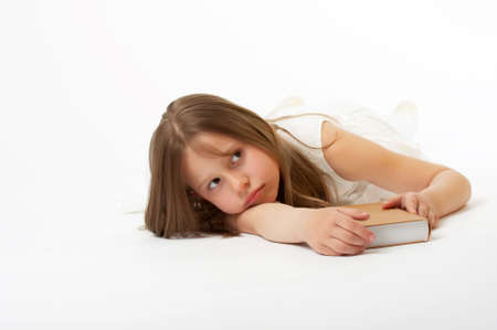 The little girl lays on a white background and discontentedly holds the bookの写真素材