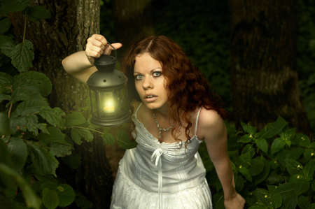 The girl with a lantern restlessly looks on a background of a twilight woodの写真素材