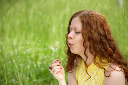 The attractive girl blows on a dandelion on a background of a lawnの写真素材