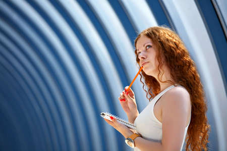 The attractive girl thoughtfully looks and holds a notebook and the pen in handsの写真素材