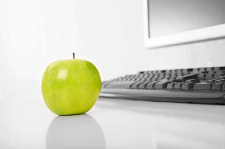 The green apple is on a table on a background of the keyboard and the monitorの写真素材