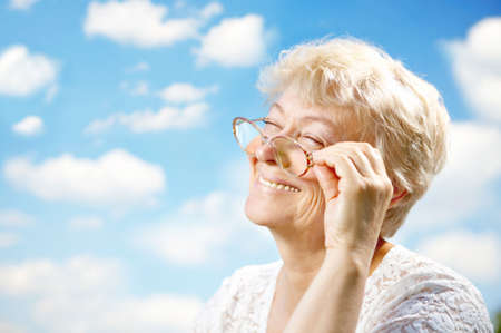 Portrait of the laughing elderly woman with glasses against the skyの写真素材