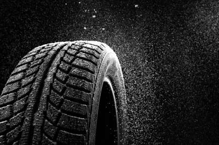 Snow sweeps up a winter tyre cover on a black backgroundの写真素材