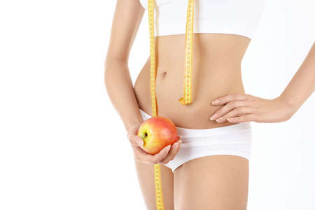 Close up in front of a beautiful female body, a measuring tape and an apple in handsの写真素材