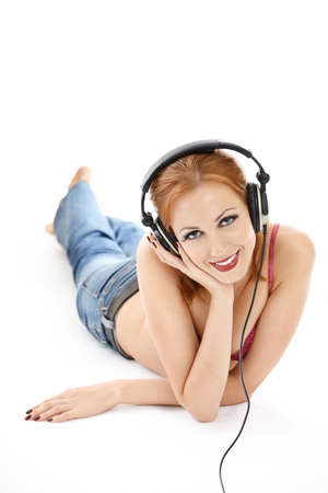 Bright girl in ear-phones lying enjoys musicの写真素材