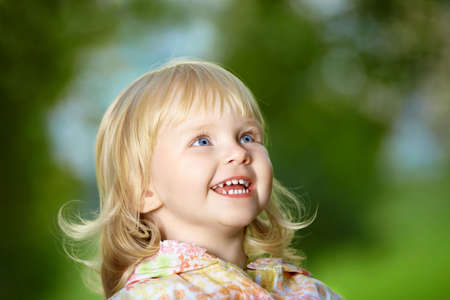 Portrait - small amusing blonde girl laughs in park
