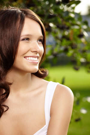 Portrait of fine young woman with curly hair against a summer gardenの写真素材