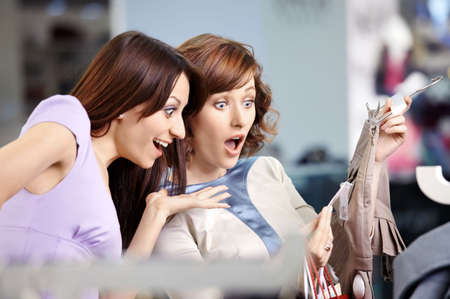 Two surprised girl-friends laugh in clothes shopの写真素材