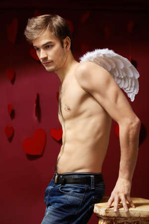 Man with naked torso and wings behind the back on a red backgroundの写真素材