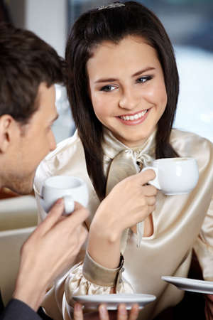 Man and woman in cafe drink coffee and smile, looking against each otherの写真素材