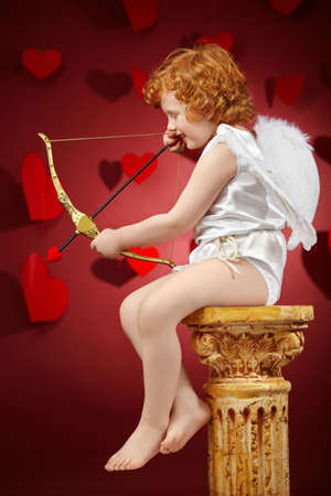 Profile of the small aiming boy - the cupid on a red backgroundの写真素材