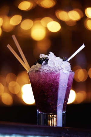 Blackberry cocktail with ice in a glass with a straw