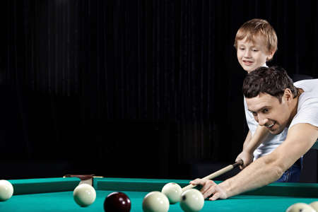 Young father and the son play billiards
