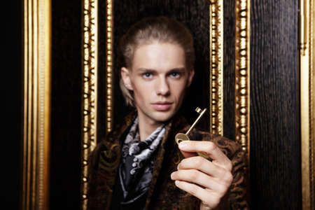 The young man holds a key against a gold doorの写真素材