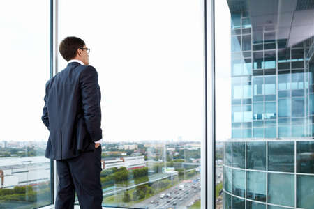 Businessman looking out of his office on the opposite buildingの写真素材