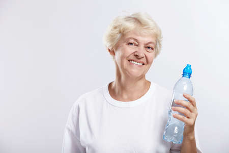 An elderly woman with a bottle of drinking water on a white backgroundの写真素材