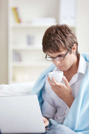 A young man in a plaid with a cup of looking at laptopの写真素材