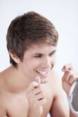 A man with dental floss at the mirror in the bathroomの写真素材