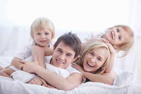 A happy family on white bed in the bedroomの写真素材