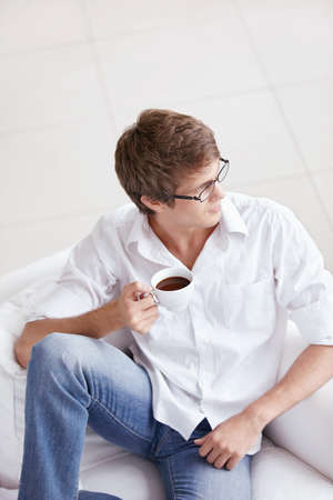 A young man with a cup of coffee on the couchの写真素材