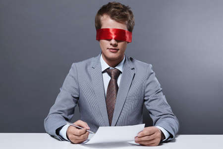 A young businessman signs a contract with a blindfoldの写真素材