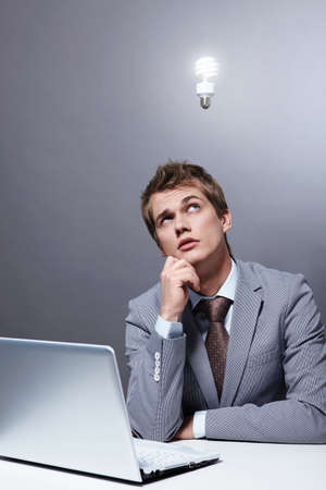A young businessman at the table looking at a burning light bulb