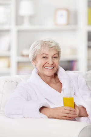 Smiling attractive woman in a bathrobe with a glass of juiceの写真素材