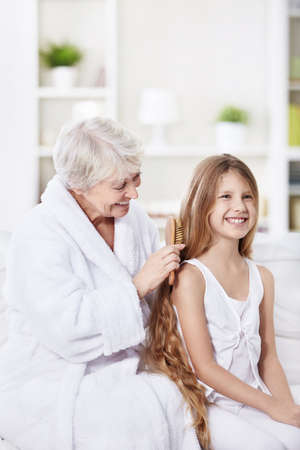 Grandmother granddaughter combs her hair at homeの写真素材