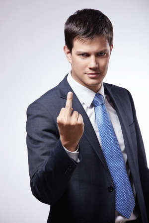 A young man in a suit shows a "fack"の写真素材