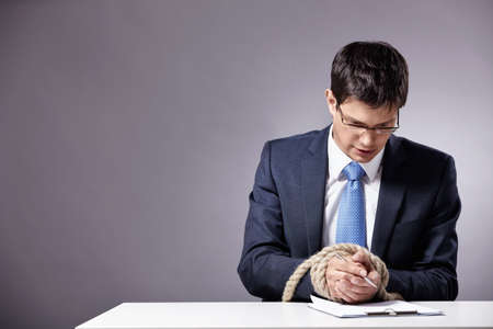 Mature businessman signs a document with tied handsの写真素材