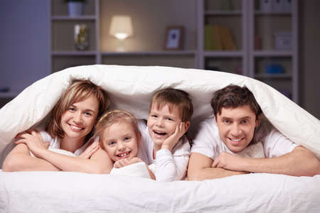 Families with children in bed under a blanketの写真素材