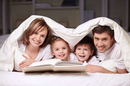 Parents with children under the blanket with a bookの写真素材