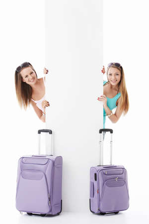 Young girls with suitcases and empty billboard on a white backgroundの写真素材