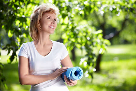 Mature woman with a gym mat in the parkの写真素材