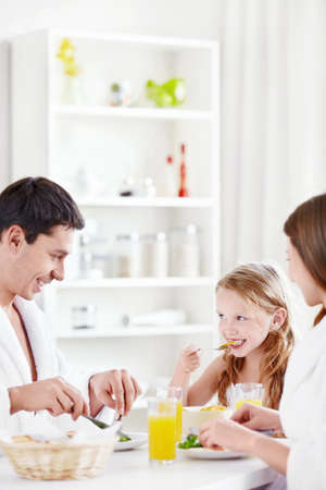 A happy family with a child eating breakfast in the kitchenの写真素材