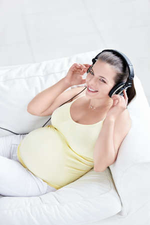 Pregnant woman with headphones on sofaの写真素材