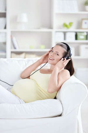 Pregnant woman with headphones at homeの写真素材