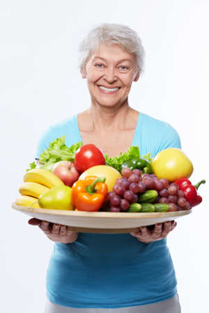 Elderly woman with fruits and vegetables on a white backgroundの写真素材