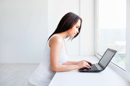 Young girl with a laptop at the windowの写真素材