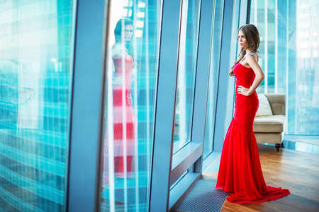 Beautiful young girl in a red dress in the apartmentの写真素材