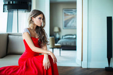 Beautiful young girl in a red dress in the apartmentの写真素材