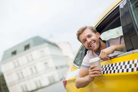Young man with coffee in a taxiの写真素材