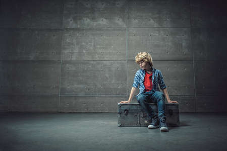 Sad boy on suitcase in studioの写真素材