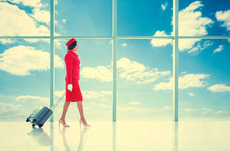 Smiling stewardess with suitcase in airportの写真素材